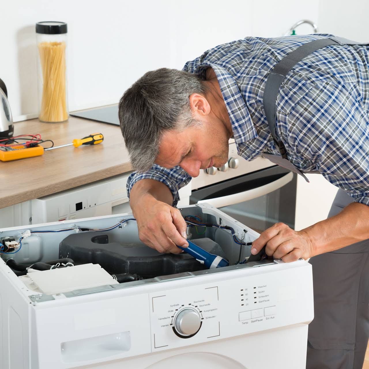 Full length of handyman checking washing machine with flashlight in kitchen